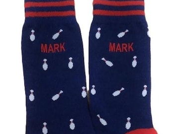 May include: A pair of blue socks with a white bowling pin pattern and red stripes at the top. The socks have the name "MARK" embroidered on them in red.