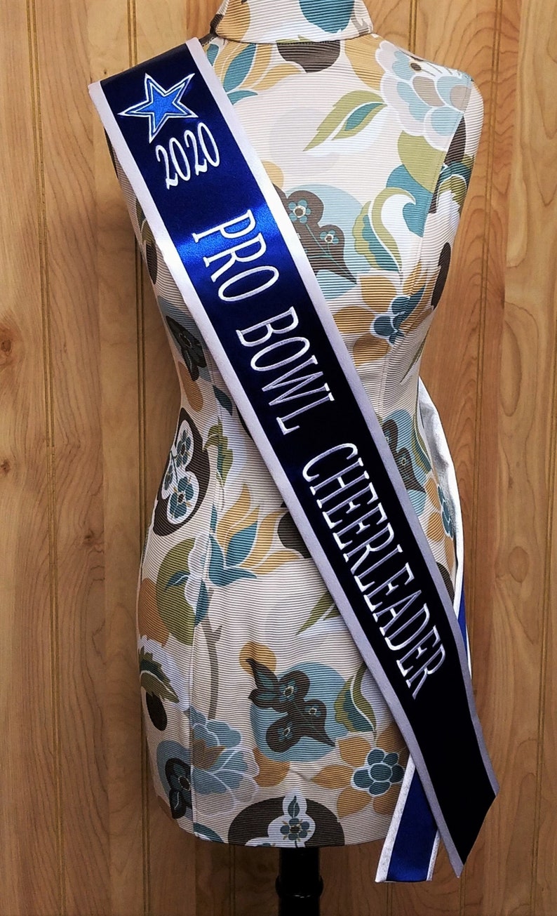 K&ouml;nnte beinhalten: Ein blaues und wei&szlig;es Band mit dem Text "2020 PRO BOWL CHEERLEADER" in wei&szlig;en Buchstaben. Ein blauer Stern befindet sich in der oberen linken Ecke des Bandes.