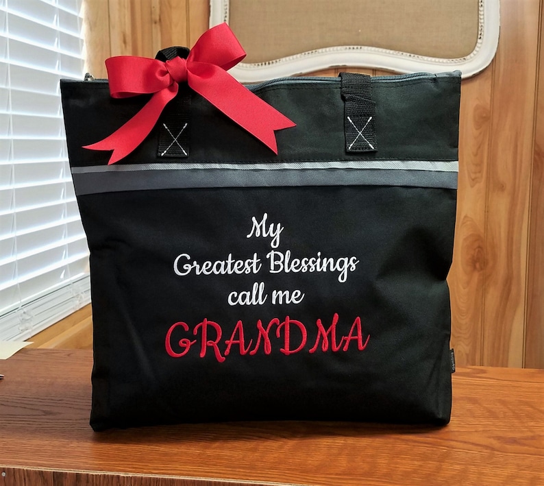 Puede incluir: Bolsa de mano negra con un lazo rojo y el texto "My Greatest Blessings call me GRANDMA" bordado en blanco y rojo.