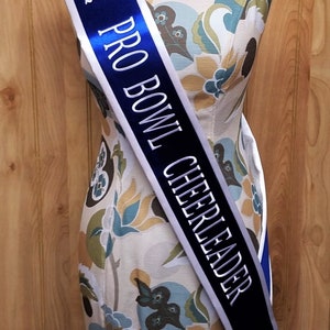 K&ouml;nnte beinhalten: Ein blaues und wei&szlig;es Band mit dem Text "PRO BOWL CHEERLEADER" und "2020" in silbernen Buchstaben. Ein blauer Stern befindet sich auf dem Band.