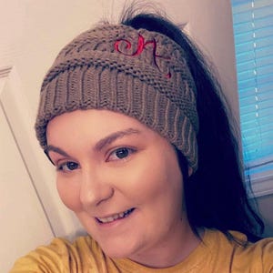 May include: A brown knit beanie with a ponytail hole and a red embroidered letter "K" on the front.
