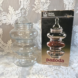 Op de afbeelding: Een doorzichtige glazen Anchor Hocking pagoda 4-delige stapelbare potset bestaande uit drie stapelbare potten en één deksel. De originele kartonnen doos is inbegrepen, met de tekst Anchor Hocking, pagoda, 4 piece stacking jar set en 12 oz/355ml.