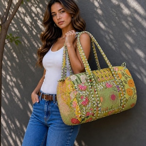 Könnte beinhalten: Eine grüne und gelbe Reisetasche mit floralen Mustern und Perlenverzierungen. Die Tasche hat zwei Griffe und eine rechteckige Form. Die Tasche wird von einer Person getragen, die ein weißes Tanktop, blaue Jeans und einen braunen Gürtel trägt.