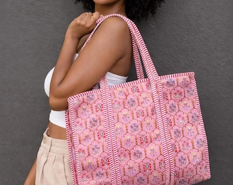 May include: A pink tote bag with a floral pattern and striped accents. The bag has two handles and is made of a textured fabric. The bag is approximately 16 inches wide and 14 inches tall.