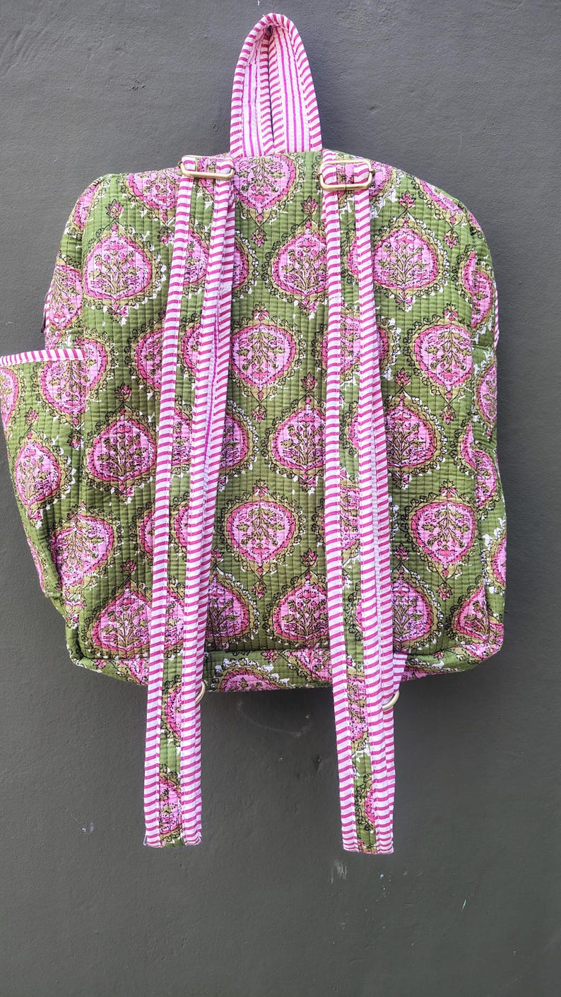 May include: A quilted backpack with a green background and a pink floral pattern. The straps and handle are pink and white striped. The backpack has a side pocket and adjustable straps.