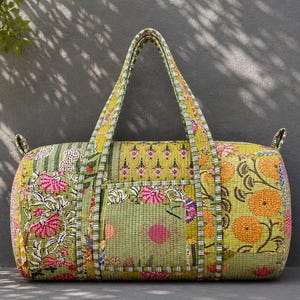 May include: A patterned duffel bag with a rectangular shape. The bag features floral and geometric designs in green, pink, and orange. It has two handles and a small pocket on the front. The bag is made of fabric.