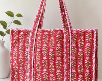 May include: A rectangular quilted tote bag featuring a vibrant red background with a repeating vertical pattern of pink flowers and green leaves. The bag includes two long handles and edge piping, all finished in a white and red striped fabric.