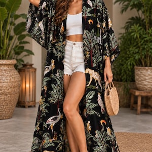 May include: A long, open-front kimono featuring a black background with a vibrant jungle print. The pattern includes illustrations of leopards, tropical birds, and palm trees in shades of green, yellow, white, and orange. The garment has wide sleeves.