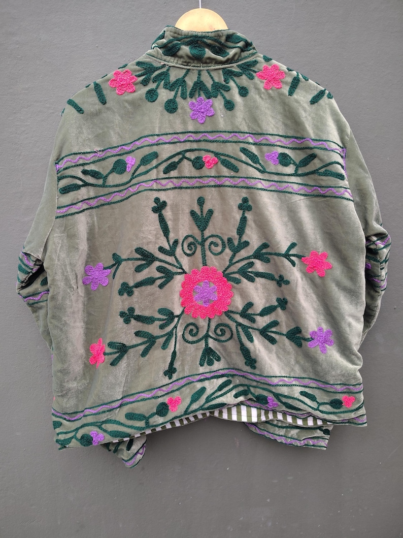 Pode incluir: Uma jaqueta verde-s&aacute;lvia com bordados florais em verde escuro, rosa choque e roxo. O design inclui um grande motivo floral central, faixas horizontais com vinhas e pequenas flores. A jaqueta tem gola alta e forro listrado.