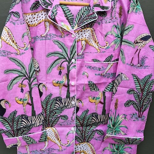 Puede incluir: Conjunto de pijama rosa con estampado tropical con leopardos, cebras, tucanes y palmeras. La parte superior de manga larga tiene ribetes blancos y botones. La tela es un material suave y ligero.