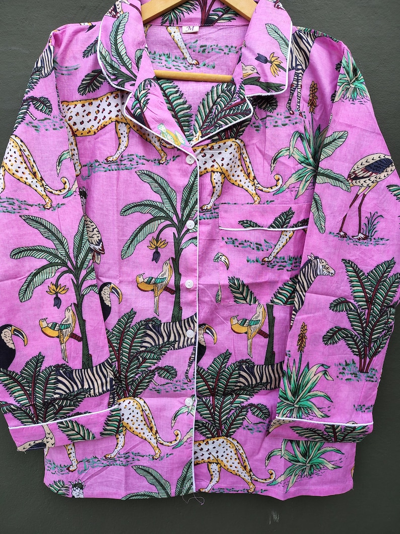 Puede incluir: Conjunto de pijama rosa con estampado tropical con leopardos, cebras, tucanes y palmeras. La parte superior de manga larga tiene ribetes blancos y botones. La tela es un material suave y ligero.