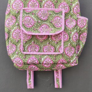 May include: A quilted backpack with a green background and a pink floral pattern. The backpack has a front pocket and pink and white striped trim. The straps and top handle are also pink and white striped.