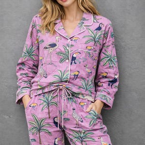 Puede incluir: Conjunto de pijama de dos piezas en tono lila claro, adornado con un estampado tropical con tucanes, cebras y palmeras. La parte superior de manga larga y los pantalones tienen ribetes blancos. Los pantalones tienen cintura con cord&oacute;n.