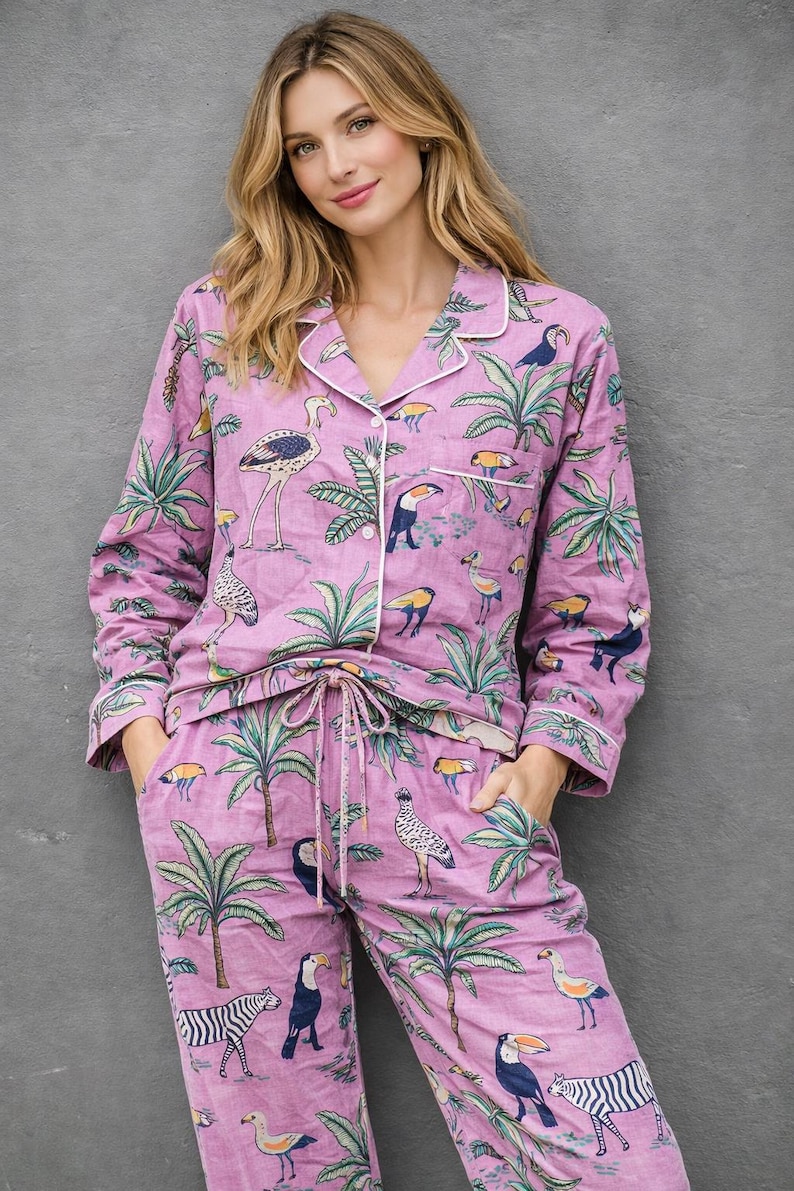Puede incluir: Conjunto de pijama de dos piezas en tono lila claro, adornado con un estampado tropical con tucanes, cebras y palmeras. La parte superior de manga larga y los pantalones tienen ribetes blancos. Los pantalones tienen cintura con cord&oacute;n.