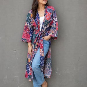 Könnte beinhalten: Ein langärmeliger, wadenlanger Kimono-Mantel mit einem lebendigen Patchwork-Muster aus verschiedenen Blumen- und geometrischen Drucken in Rot-, Blau-, Grün- und Weißtönen. Das Kleidungsstück verfügt über einen passenden Bindegürtel.