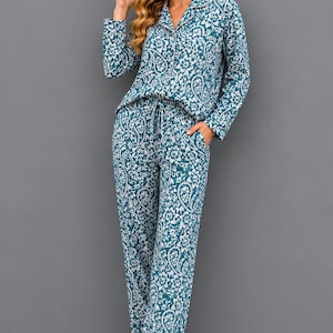 Könnte beinhalten: Türkisblaues und weißes Paisley-Pyjama-Set. Das langärmlige Oberteil hat einen gekerbten Kragen und einen Knopfverschluss. Die Hose hat einen Kordelzug in der Taille und Taschen. Der Stoff hat ein Blumenmuster.
