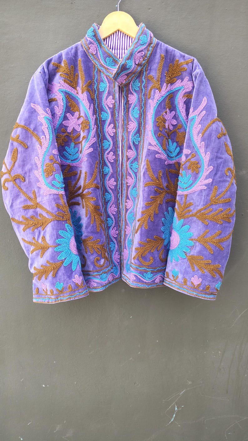 May include: A purple velvet jacket with intricate embroidery in shades of brown, teal, and pink. The jacket features a high collar and a full zipper. The lining is striped. This jacket is a unique piece of outerwear.