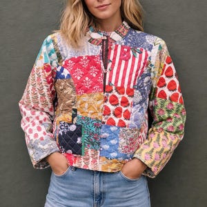 Könnte beinhalten: Eine Patchwork-Jacke mit einer Vielzahl farbenfroher Muster, darunter Blumen-, Streifen- und geometrische Designs. Die Jacke hat einen Stehkragen, einen Reißverschluss und lange Ärmel. Getragen mit blauen Jeans.