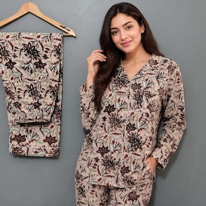 Könnte beinhalten: Ein zweiteiliger Schlafanzug bestehend aus einem langärmeligen Hemd mit Knopfleiste und einer passenden Hose. Der Stoff ist hellbeige mit einem dichten Blumen- und Blattmuster in Dunkelbraun und gedecktem Grün. Das Hemd hat einen Reverskragen und eine Tasche.