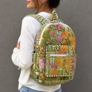 Könnte beinhalten: Grüner Rucksack mit floralem Muster, weißen Reißverschlüssen und einer Vordertasche. Der Rucksack hat eine gesteppte Textur und zeigt orangefarbene und rosa Blumendesigns. Die Träger sind grün und weiß gestreift.