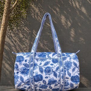 Könnte beinhalten: Blau-weiß bedruckte Tragetasche mit floralem Muster und passenden Griffen. Die Tasche hat ein gestepptes Design und einen Reißverschluss. Die Griffe sind blau und weiß gestreift. Die Tasche ist aus einem weichen, strapazierfähigen Stoff gefertigt.