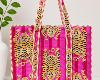 May include: A quilted tote bag featuring a vibrant hot pink background with vertical stripes and a repeating pattern of yellow and black tigers. The bag includes two long handles with orange and white striped trim, matching the piping along the edges.