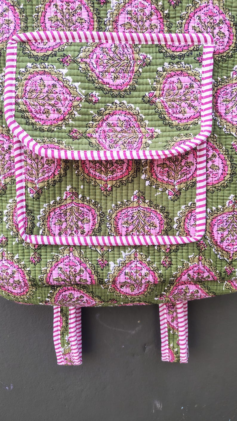 May include: Close-up of a quilted tote bag with a green background and a pink floral pattern. The bag has two pockets and a pink and white striped trim. The handles are also pink and white striped.