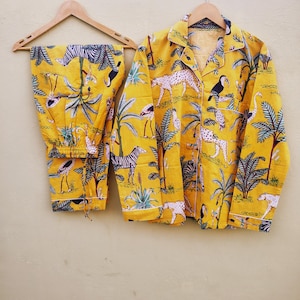 Pu&ograve; includere: Pigiama giallo con stampa di animali della giungla, tra cui zebre, leopardi e tucani. Il set comprende una camicia con bottoni e pantaloni abbinati, appesi a una gruccia di legno.