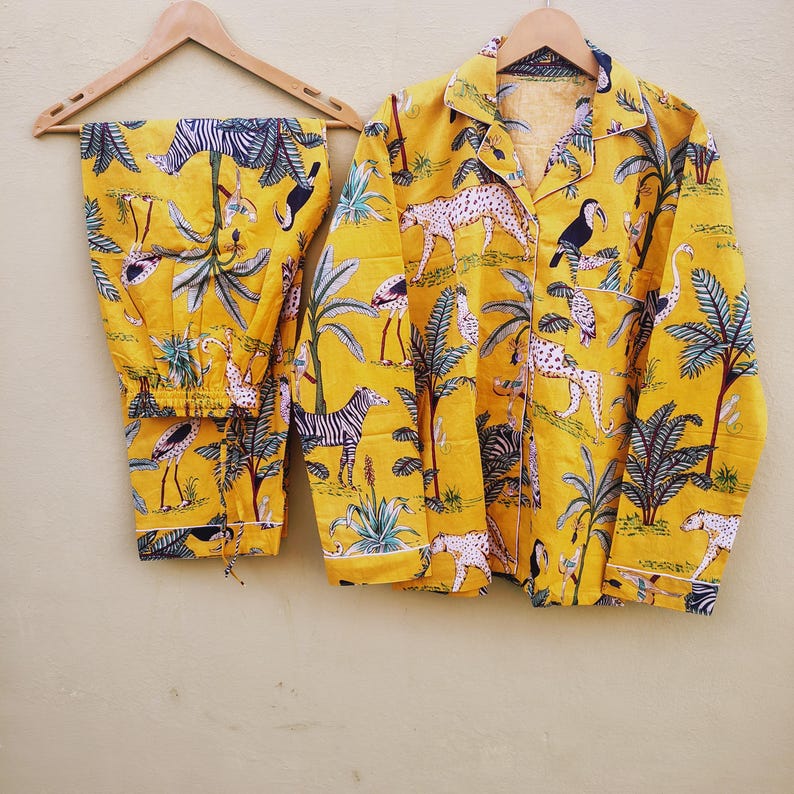 Pu&ograve; includere: Pigiama giallo con stampa di animali della giungla, tra cui zebre, leopardi e tucani. Il set comprende una camicia con bottoni e pantaloni abbinati, appesi a una gruccia di legno.