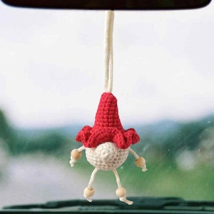 May include: A red and white crocheted gnome hanging from the rearview mirror of a car. The gnome has a red hat and a white beard. The text "Wooly Smile" is visible in the upper right corner of the image.