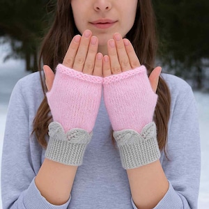 Op de afbeelding: Roze gebreide vingerloze handschoenen met grijze manchetten en decoratieve details. De handschoenen zijn gemaakt van zacht, getextureerd garen en zijn ontworpen om de handen warm te houden terwijl de vingers vrij blijven. Een gezellig accessoire.