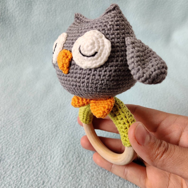 May include: A gray crocheted owl rattle with orange and green accents attached to a wooden ring.
