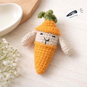 May include: A handmade crochet carrot-shaped bunny with a smiling face. The bunny is primarily cream and orange, with green leaves on top. The text "Click-Clack" is in a black oval.