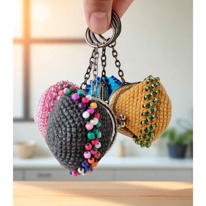 Puede incluir: Una colecci&oacute;n de monederos de ganchillo hechos a mano en varios colores, incluyendo rosa, gris, azul y amarillo. Cada monedero est&aacute; adornado con cuentas y unido a un llavero. Los monederos son sostenidos por una mano.