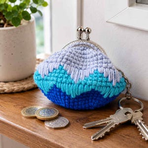 May include: A small, crocheted coin purse featuring a wave-like pattern in shades of light blue, turquoise, and dark blue. The purse has a silver-toned metal kiss-lock clasp and an attached silver metal keyring with two keys.
