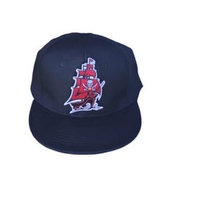 May include: A navy blue baseball cap featuring a red pirate ship logo with a skull and crossbones. The cap has a flat brim and a structured crown, suitable for sports or casual wear.