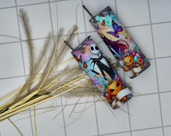 May include: Two tall, colorful tumblers with black straws. One features Jack Skellington from The Nightmare Before Christmas, the other has a whimsical design with butterflies and pumpkins. Both are set against a light background with decorative grass.