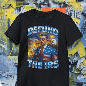 May include: Black t-shirt with a graphic that reads "DEFUND THE IRS." The graphic features a man in a suit, sunglasses, and a cigar, with an American flag and an eagle in the background.