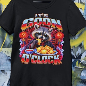 May include: A black short-sleeve t-shirt featuring a graphic of a raccoon wearing sunglasses and eating a fried wonton. The text reads IT'S GOON O'CLOCK. The design includes red lanterns, a plate of wontons, and a small bowl of dipping sauce.