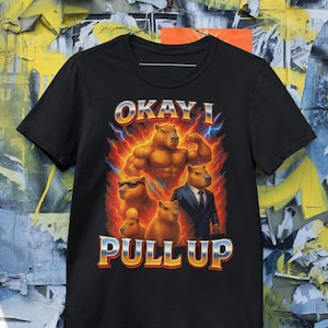 May include: Black t-shirt with a graphic featuring capybaras in various poses, including one flexing and another in a suit. The text "OKAY I PULL UP" is displayed in a stylized font with lightning bolts.