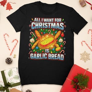 Könnte beinhalten: Schwarzes T-Shirt mit einem festlichen Grafikdesign. Das Design zeigt ein Cartoon-Knoblauchbrot, umgeben von Zuckerstangen, Lichtern und dem Text "ALL I WANT FOR CHRISTMAS IS GARLIC BREAD."