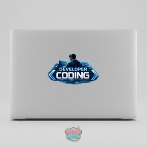 Pode incluir: Um laptop branco com um adesivo com um desenvolvedor codificando. O adesivo mostra uma pessoa com fones de ouvido trabalhando em um computador, com as palavras "DEVELOPER CODING" em azul.