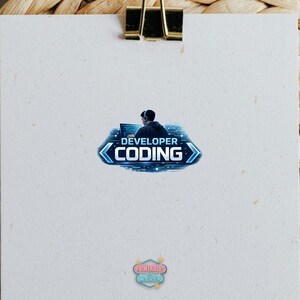 Pode incluir: Um papel branco com um clipe dourado no topo. O papel tem um gr&aacute;fico azul e branco de uma pessoa codificando, com as palavras "DEVELOPER CODING". Na parte inferior h&aacute; um pequeno logotipo que diz "Printables Marek".