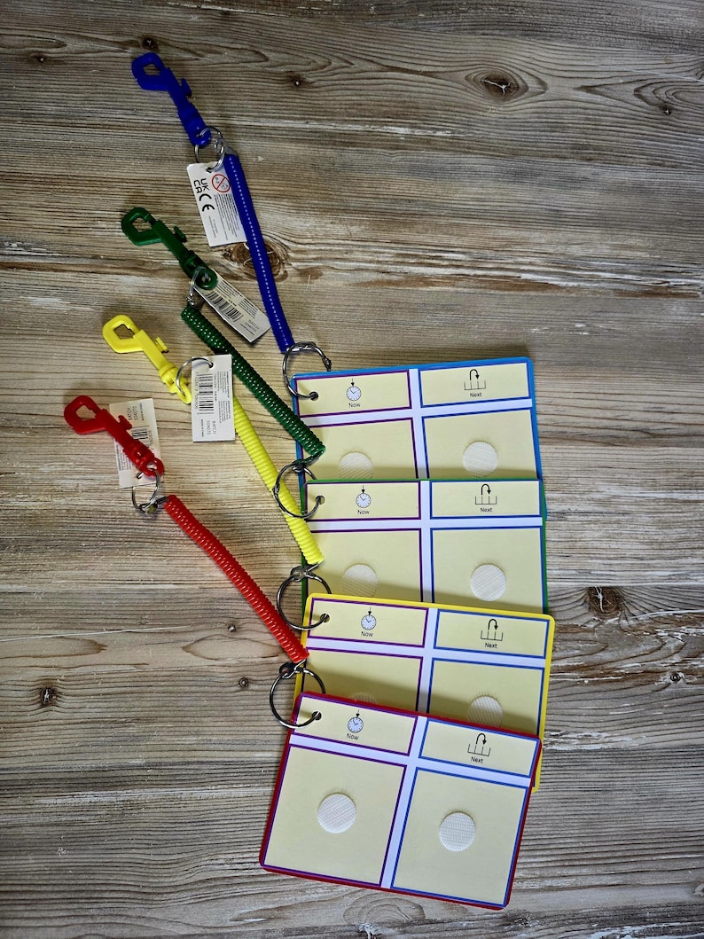 May include: A set of colorful communication boards with matching coiled lanyards. The boards are yellow, green, and blue, with white circles and the words "Now" and "Next". The lanyards are red, yellow, green, and blue.
