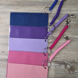 May include: A set of five rectangular plastic cards in a gradient of blue, purple, and pink shades, each attached to a matching colored coiled wristband with a metal split ring and a silver-toned lobster clasp for secure attachment.