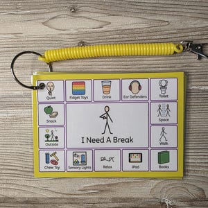 May include: A yellow plastic coil keychain attached to a rectangular communication card featuring a central stick figure illustration labeled I Need A Break, surrounded by twelve smaller icons representing activities like snack, outside, chew toy, and iPad.