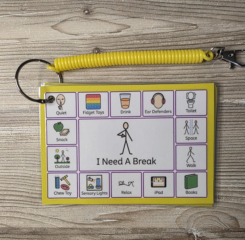 May include: A yellow plastic coil keychain attached to a rectangular communication card featuring a central stick figure illustration labeled I Need A Break, surrounded by twelve smaller icons representing activities like snack, outside, chew toy, and iPad.