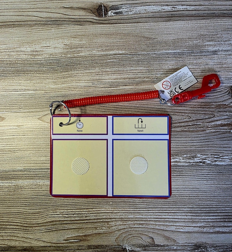 May include: A red and yellow communication board with the words "Now" and "Next" printed on it. The board has a red border and a red coiled lanyard attached to it. The lanyard has a red plastic clip.
