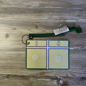 May include: A green and yellow communication board with the words "Now" and "Next". The board has a spiral cord and a green handle. The board has a hook and loop fastener.