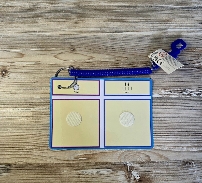 May include: A visual aid card with a blue border and a blue spiral cord. The card has two sections with the words "Now" and "Next". Each section has a white circle. A small tag is attached.